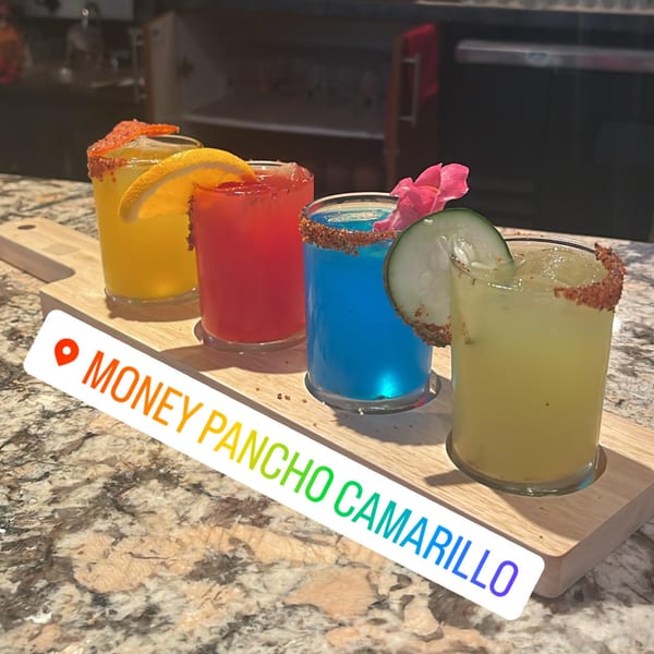 Four colorful Mexican cocktails, including yellow, red, blue, and green, on a wooden serving tray.
