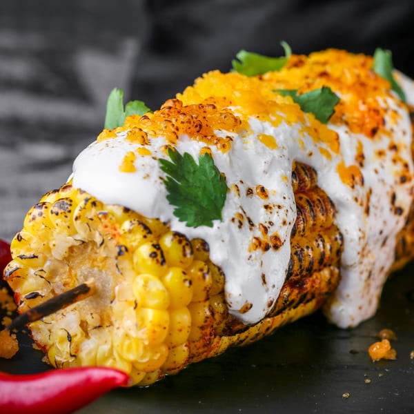 Grilled Mexican street corn (elote) with creamy white sauce, orange roe, and cilantro.
