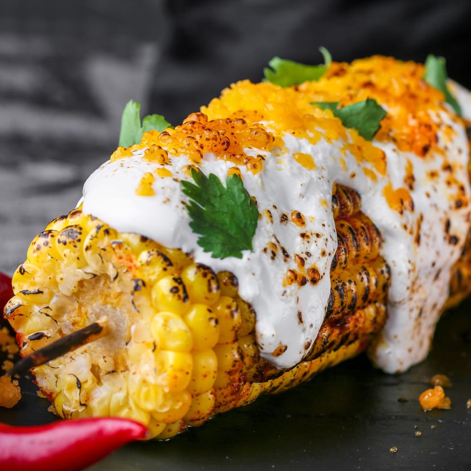 Grilled Mexican street corn (elote) with creamy white sauce, orange roe, and cilantro.